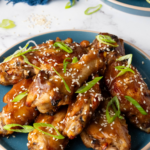 plate of glazed Chinese wings with a blue napkin in the background.