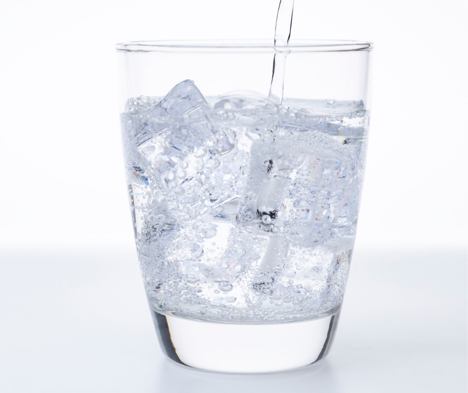 Close-up of clear, sparkling water being poured into a tumbler filled with ice cubes, creating many small bubbles.