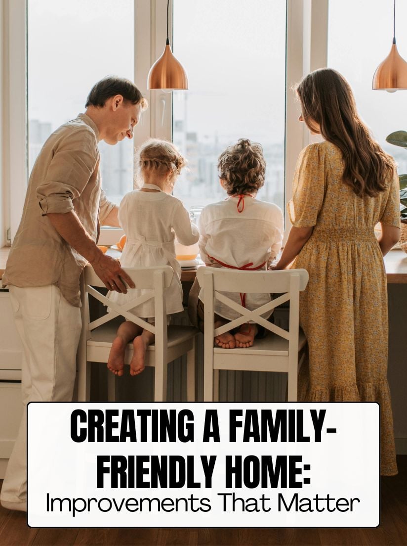 A family of four—two adults and two young children—standing together at a bright kitchen counter by a large window. The children are standing on white wooden chairs to reach the counter. Text overlay reads: "CREATING A FAMILY-FRIENDLY HOME: Improvements That Matter.