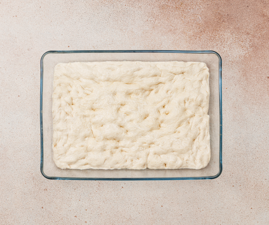 Focaccia bread dough stretched to the edges of a glass baking pan.