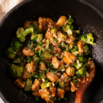 A white plate featuring a portion of honey garlic chicken and steamed broccoli florets next to a silver fork.