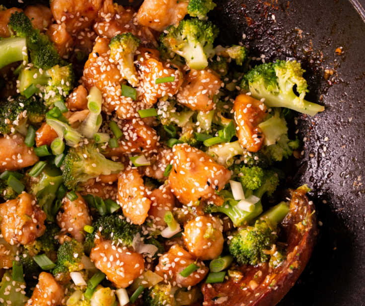 Close up of honey garlic chicken bites with sesame seeds and green onions in a wok.