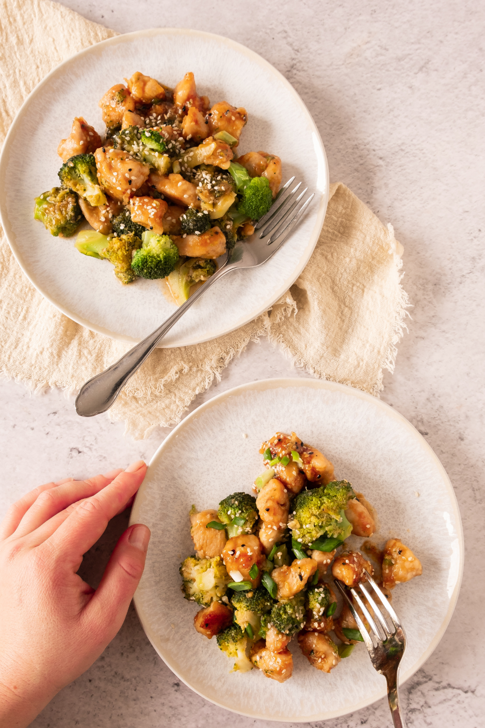 Two plates of homemade honey garlic chicken with a hand holding a fork.