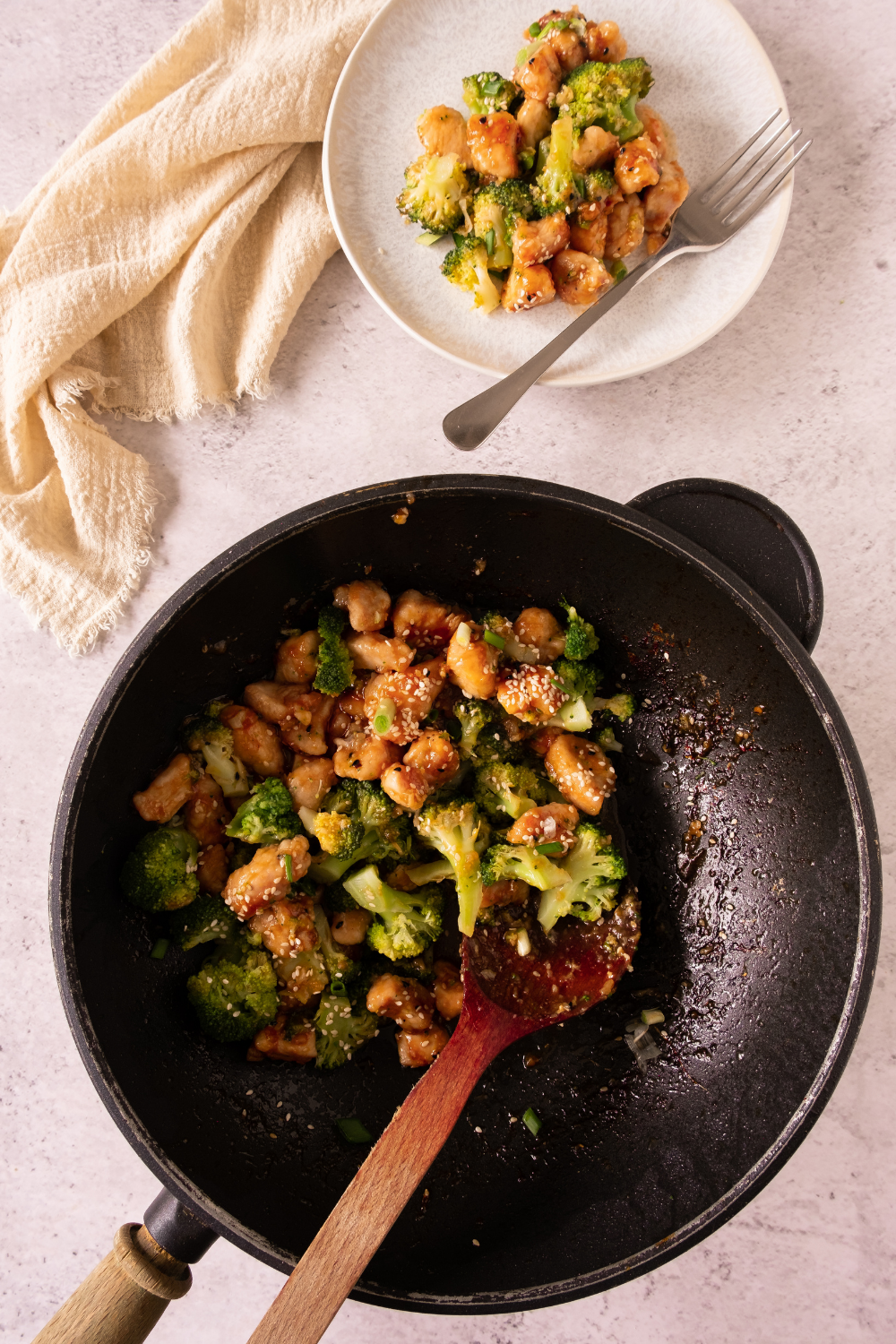 Plated honey garlic chicken and broccoli garnish with sesame seeds and green onions.