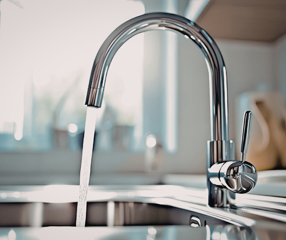 A sleek, high-arc chrome kitchen faucet with water flowing into a stainless steel sink.