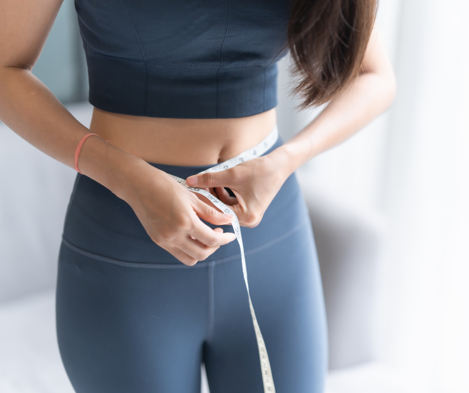 A close-up of a person in fitness apparel using a flexible white measuring tape to check their waist circumference.