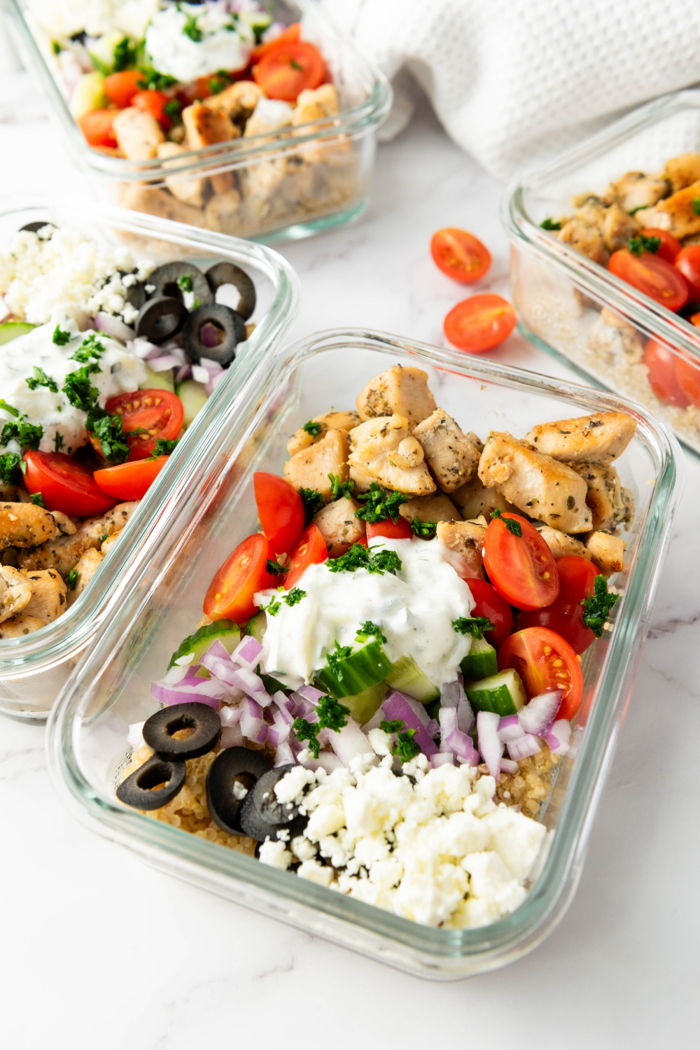 Multiple glass containers filled with Greek chicken quinoa bowls for weekly healthy meal prep.