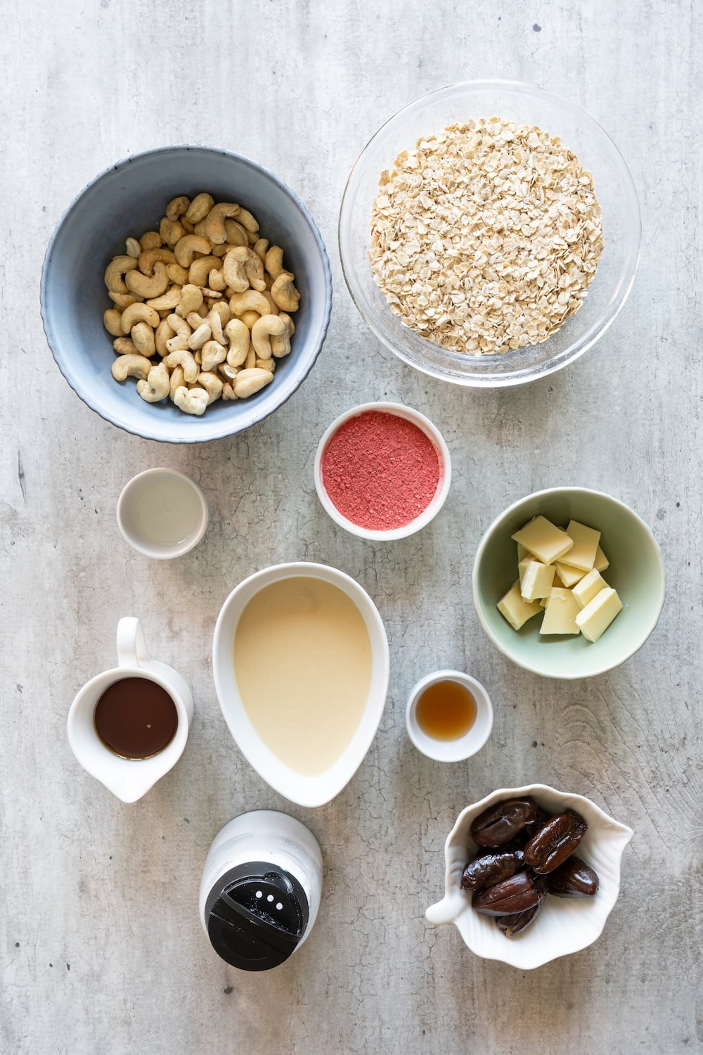 Flat lay of ingredients for strawberry energy bites including oats, cashews, almond butter, dates, maple syrup, and freeze-dried strawberry powder.