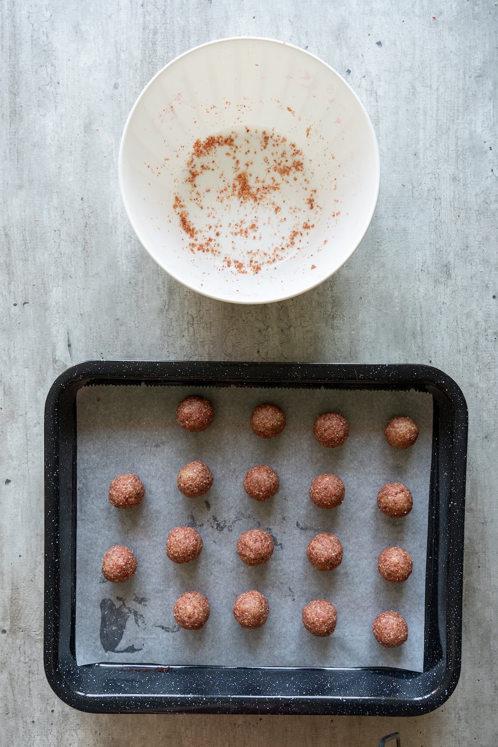 Sixteen evenly scooped strawberry oat energy balls arranged on a parchment-lined baking sheet.