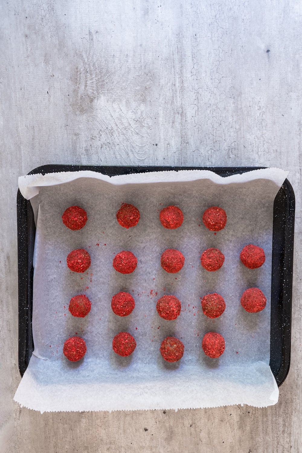 A tray of energy balls completely coated in red strawberry powder ready for drizzling.
