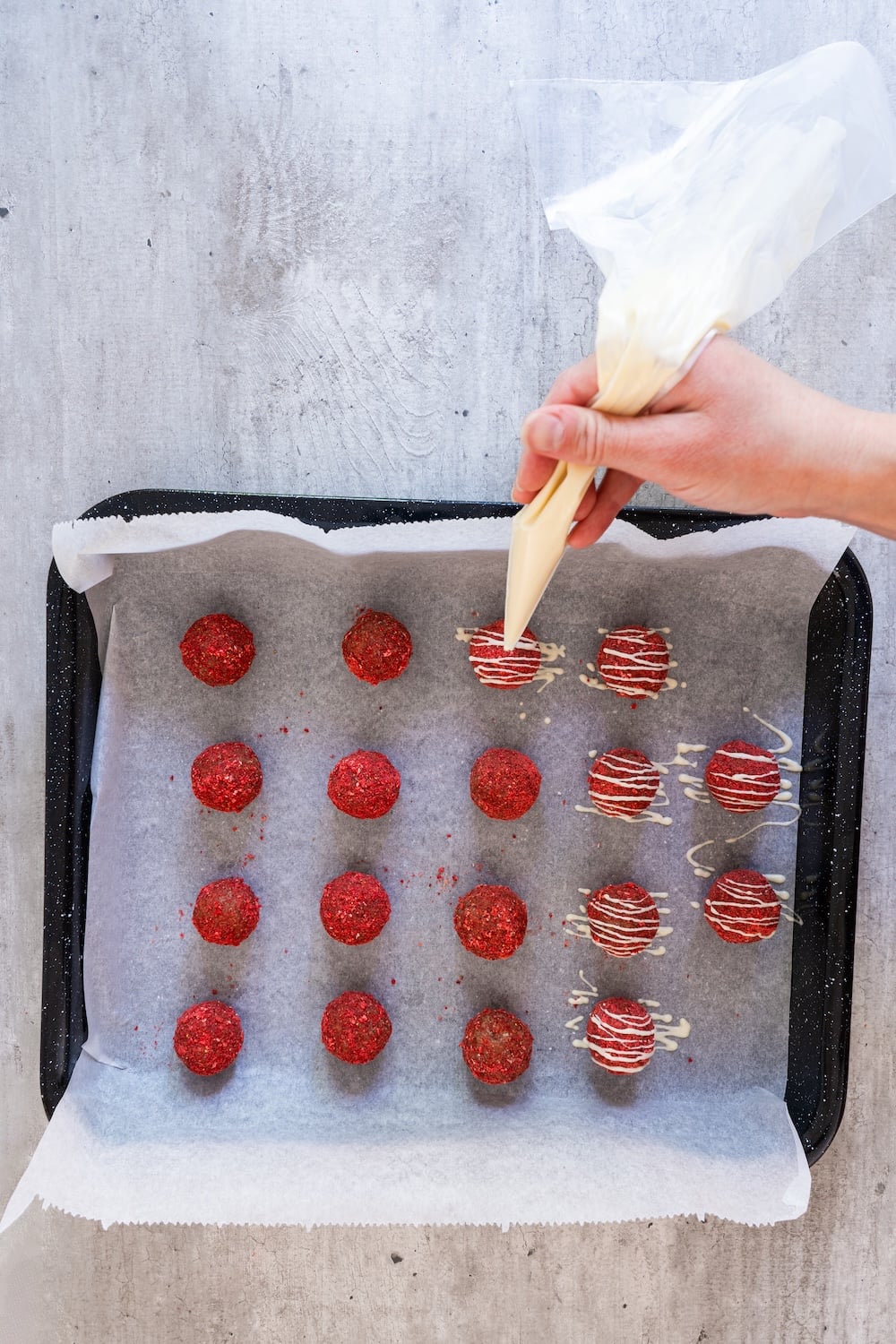 A hand using a piping bag to drizzle melted white chocolate over strawberry-coated energy bites.