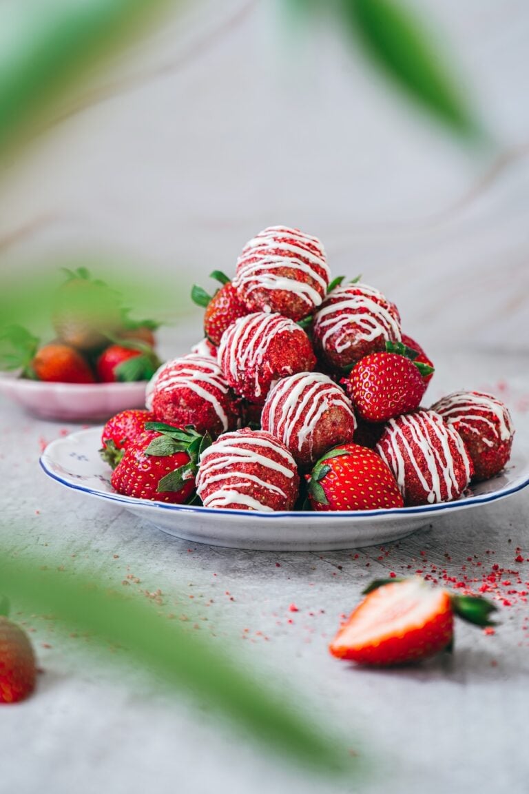 A decorative pile of strawberry shortcake energy bites on a white plate, garnished with fresh whole strawberries.