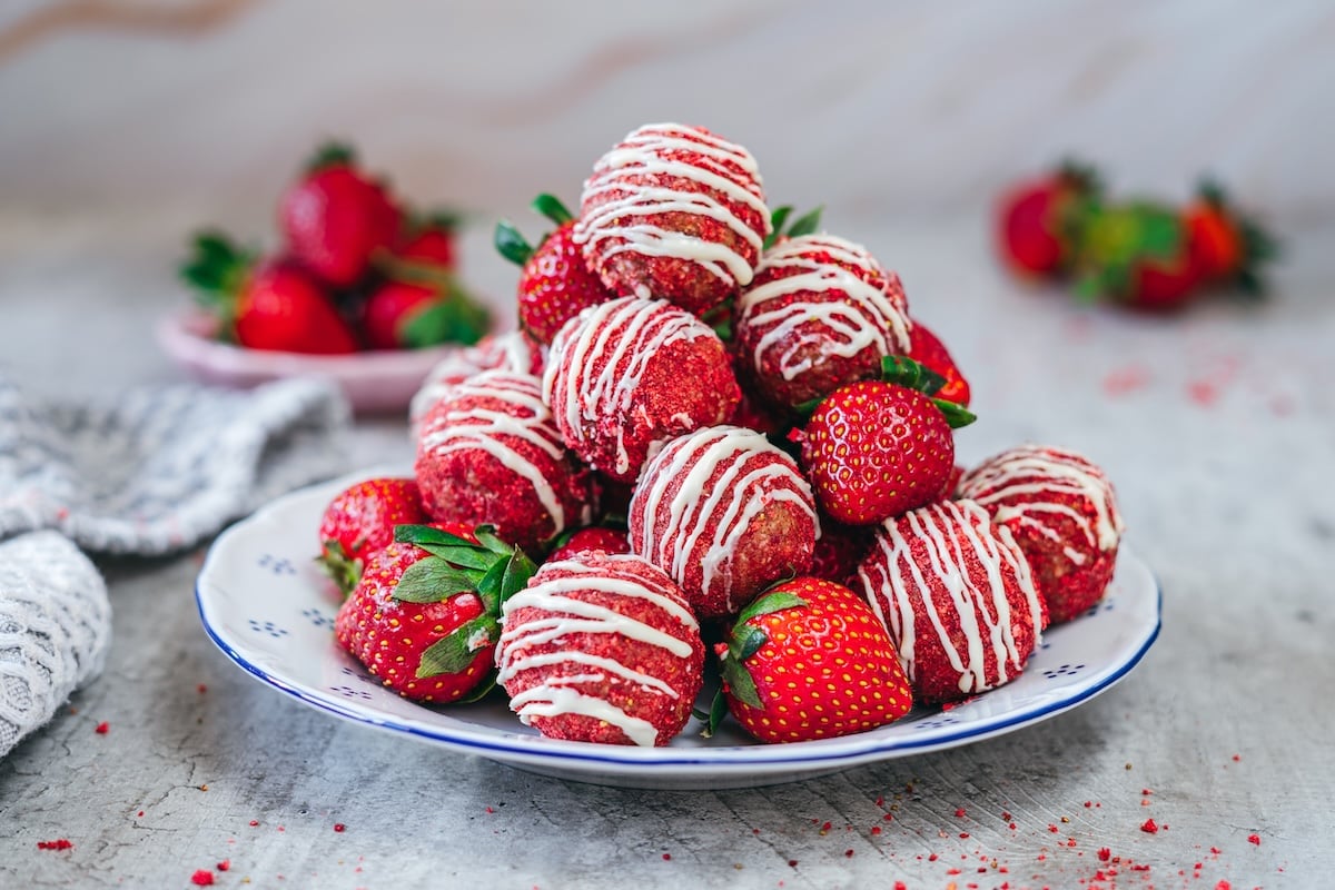 A stack of strawberry energy bites with the top one having a bite taken out, revealing a soft, nutty interior.