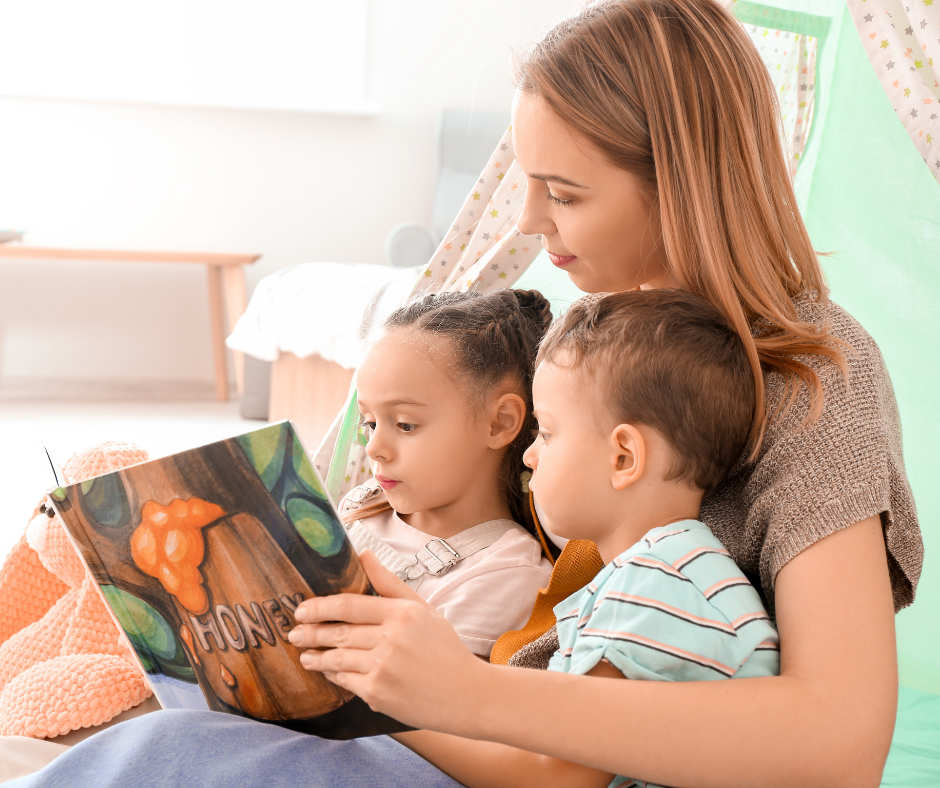 A young woman reading a picture book about honey to a young boy and girl inside a play tent.