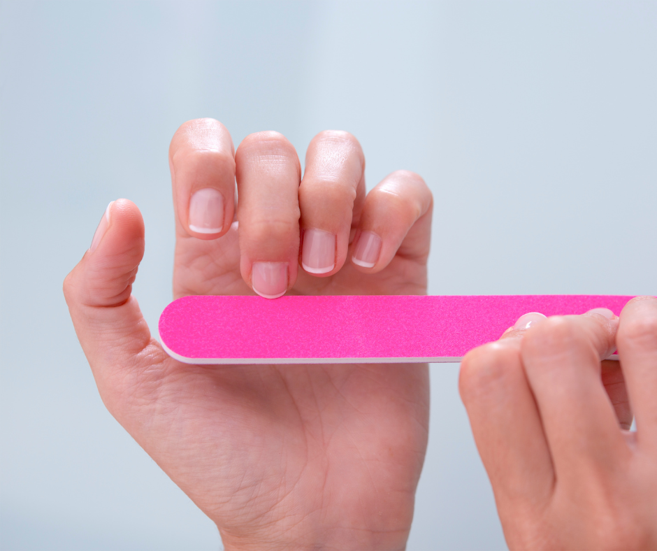 A person holding a bright pink nail file horizontally against their natural fingernails for shaping.