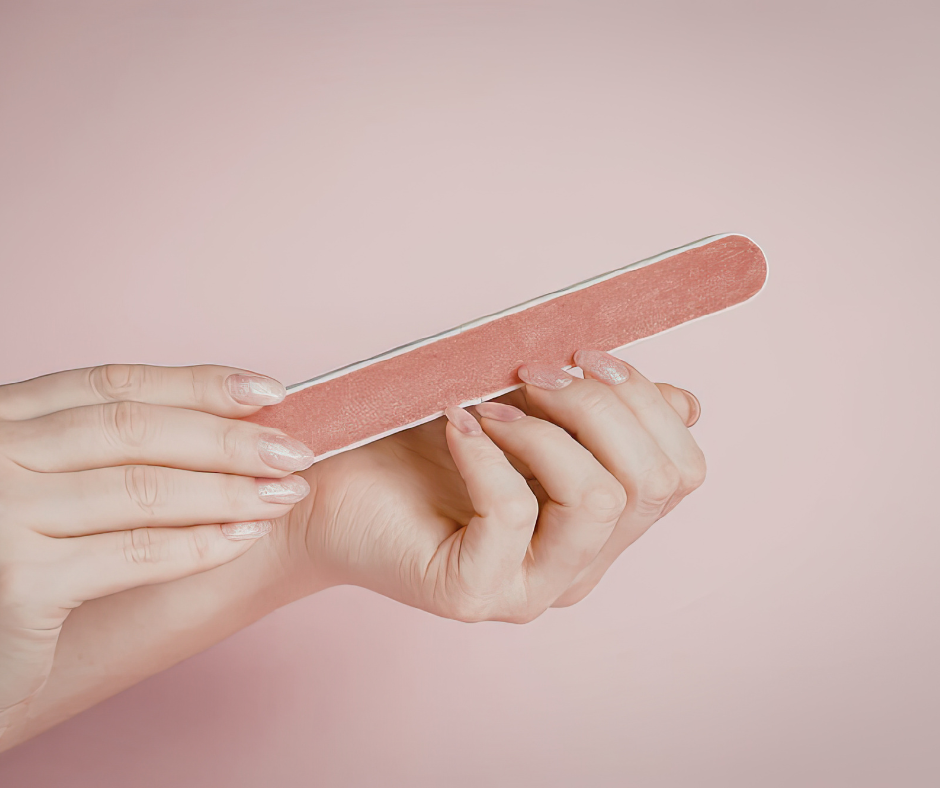 A close-up of hands holding a classic orange-brown emery board against a soft pink background.