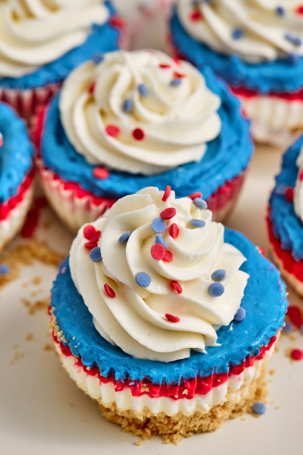 Red, white, and blue no-bake cheesecake cupcakes served on a white plate, perfect as a quick and easy dessert idea for a Fourth of July party or summer BBQ.