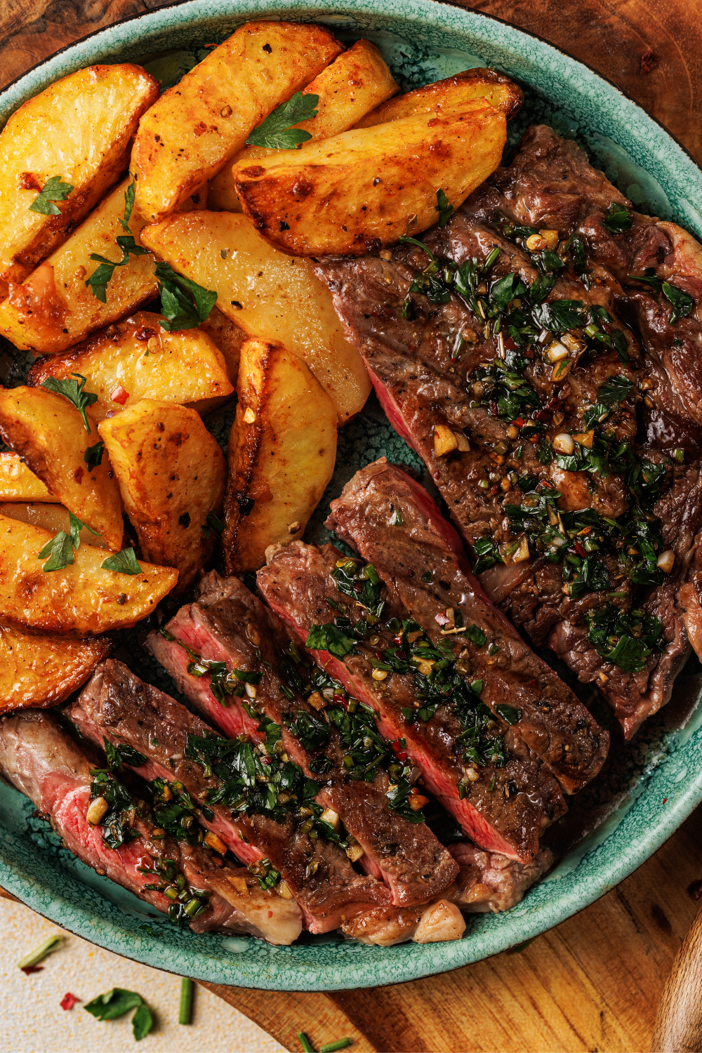 Medium-rare steak with vibrant chimichurri sauce and golden garlic fries served in a teal bowl.
