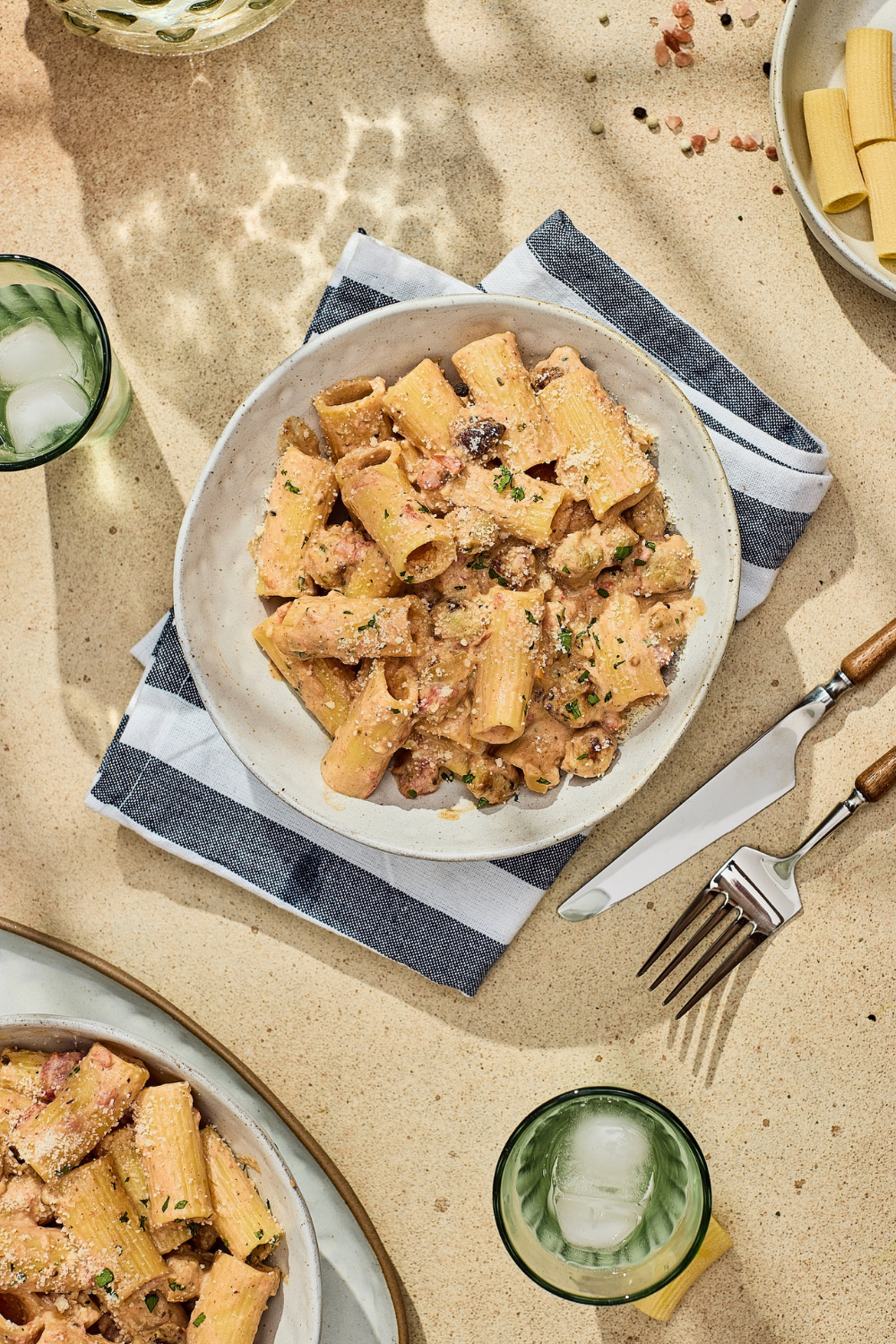 A bowl of rigatoni pasta with a creamy tomato and sausage sauce served on a blue and white striped napkin for a quick weeknight dinner.