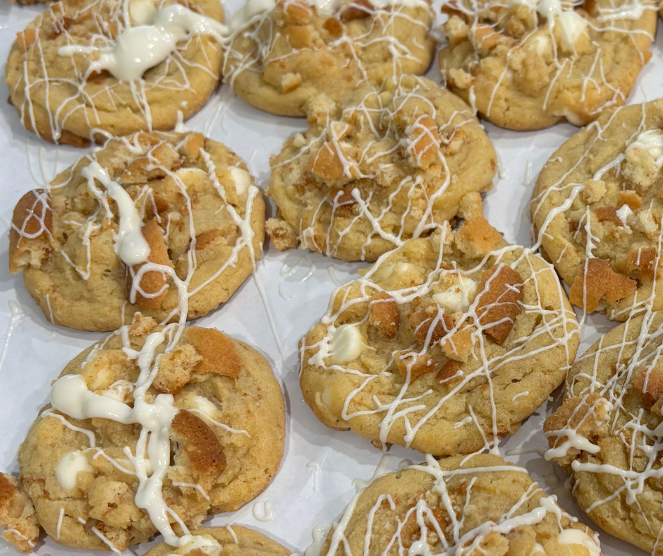 A close-up of a homemade cookie recipe for banana pudding cookies topped with white chocolate drizzle and crushed vanilla wafers.
