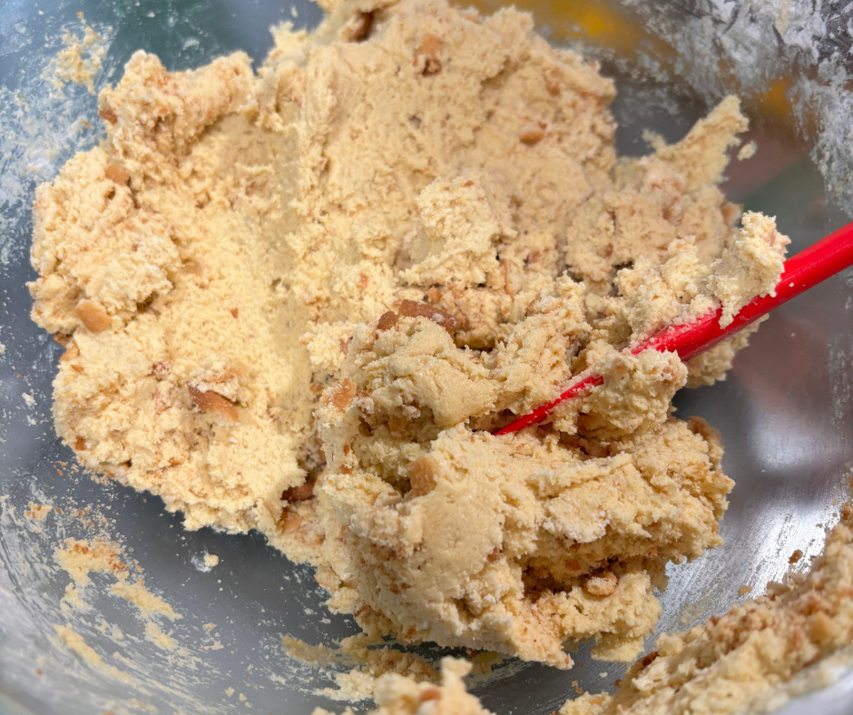 A clear mixing bowl showing how to make cookie dough for banana pudding cookies with crushed vanilla wafer pieces folded in.