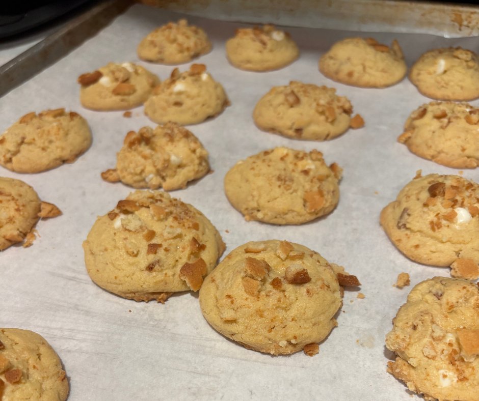 Freshly baked cookie recipes with white chocolate chip and banana flavor sitting on parchment paper before being drizzled.