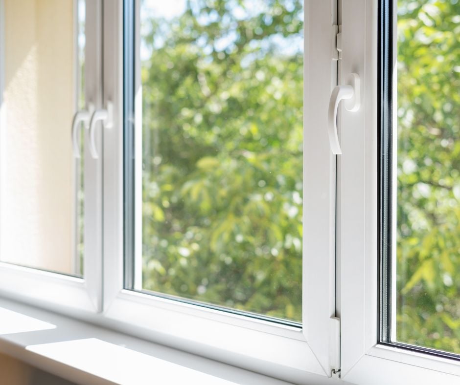 Close-up of clean, modern white vinyl window frames with open latches looking out at bright green trees on a sunny day.