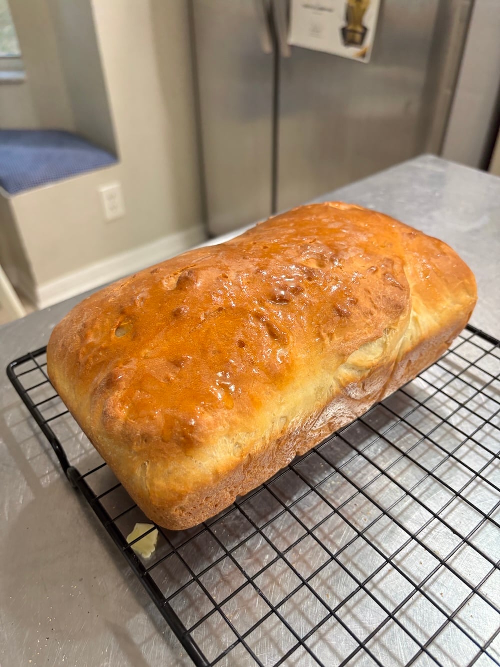 A single golden-brown loaf of homemade white bread resting on a wire cooling rack.