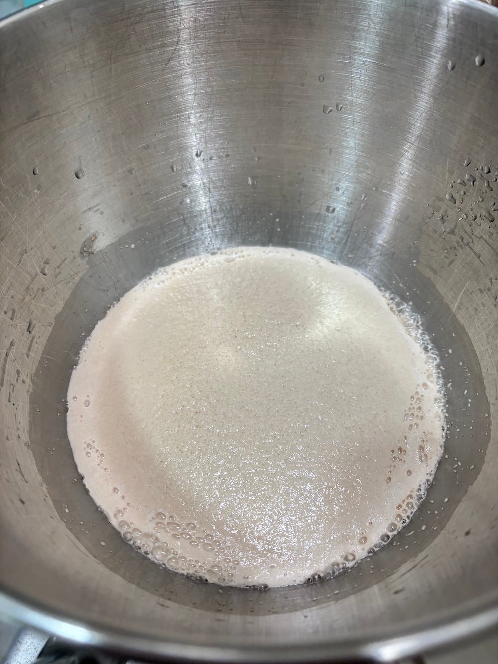 Creamy yeast foam active in a stainless steel mixer bowl.