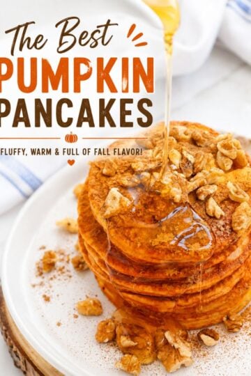 A stack of five pumpkin spice pancakes on a white plate, topped with chopped walnuts and drizzled with maple syrup. The background is a rustic wooden table with a napkin and other breakfast items, out of focus.