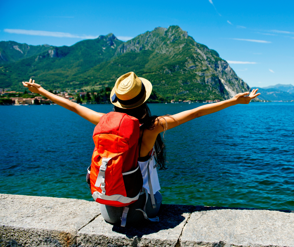 Traveler with a backpack enjoying fresh air and sunshine by a lake, representing the benefits of daylight and gentle movement after a red-eye flight.