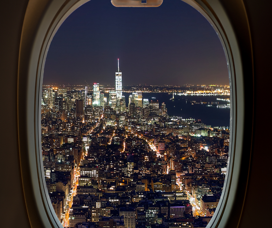 Nighttime city skyline viewed through an airplane window during a red-eye flight, highlighting overnight air travel and long-distance journeys.